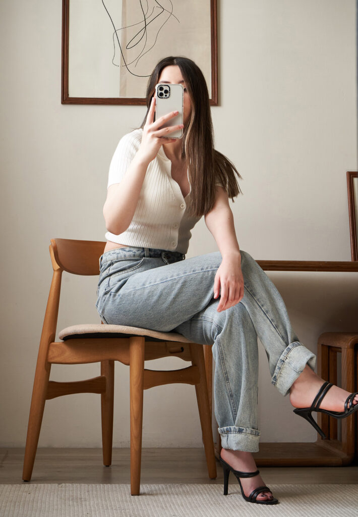 Gabriela Inzunza for Avice a modern room with minimalist decor a wooden chair a framed abstract artwork and a person taking a mirror selfie.